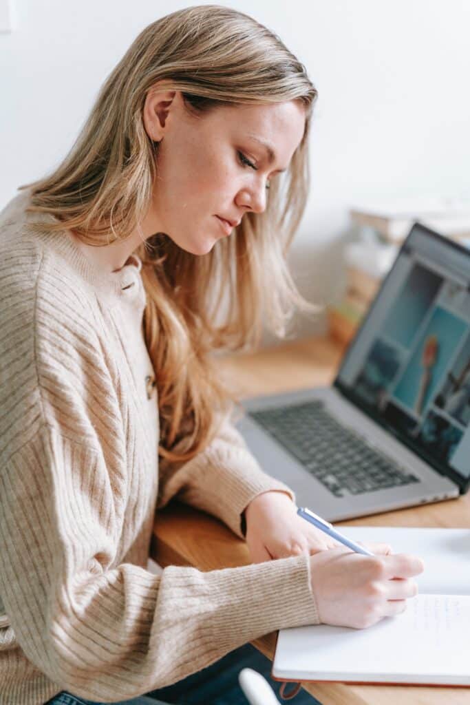 jeune femme blonde devant son ordinateur écrivant des notes sur un carnet, conciergerie Airbnb location maison appartement